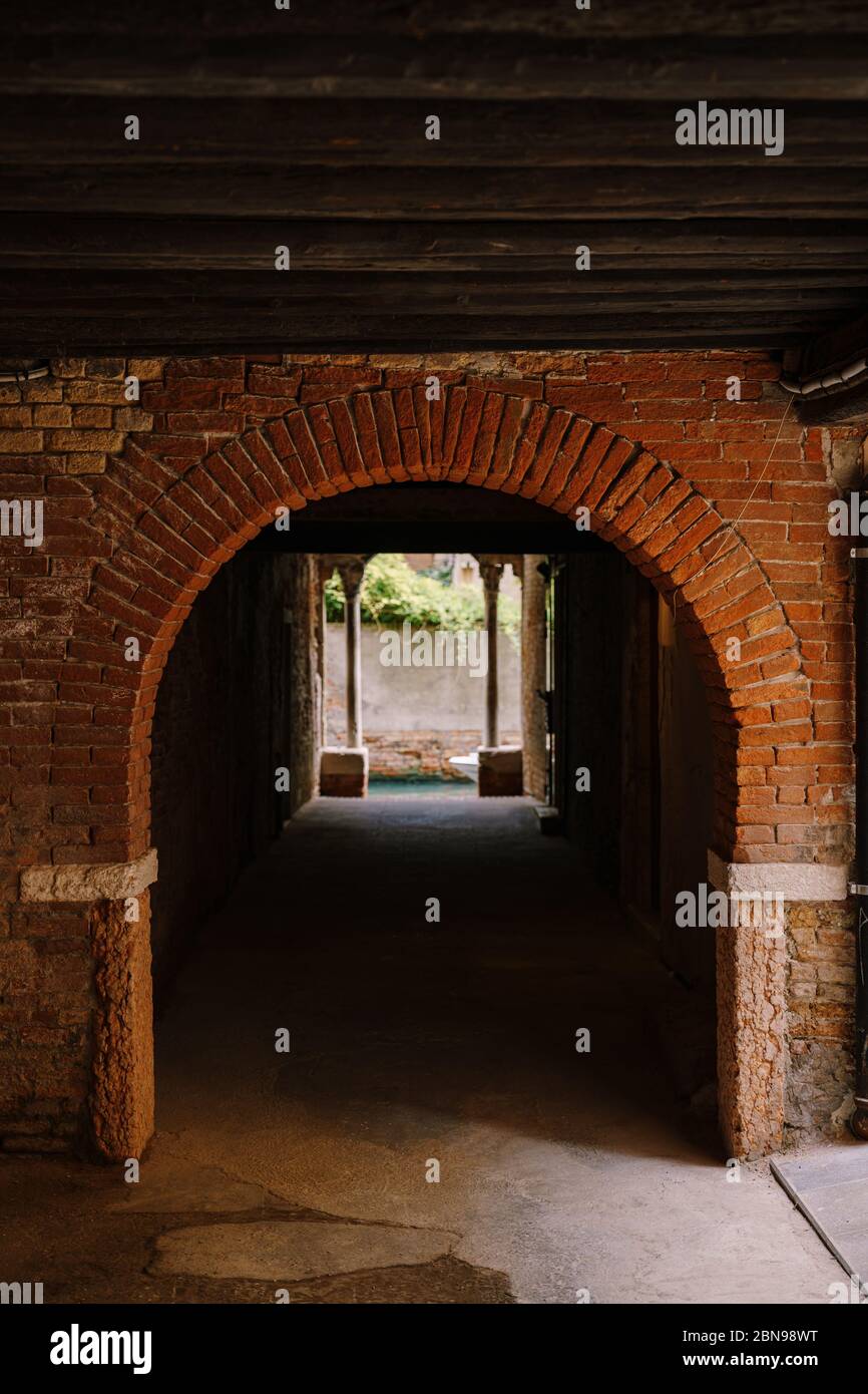 Blick vom Gebäude auf einen kleinen schmalen Kanal zwischen den Häusern in Venedig, Italien. Ein Blick aus einem Tunnel mit Backsteinwänden, zwei antiken Säulen und Stockfoto