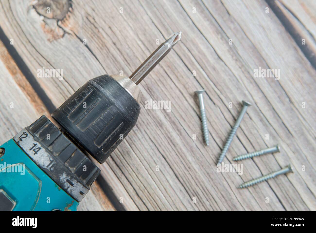 Alte Schraubendreher und Schrauben auf dem Holzhintergrund. Flache Ansicht des elektrischen Schraubendrehers Stockfoto