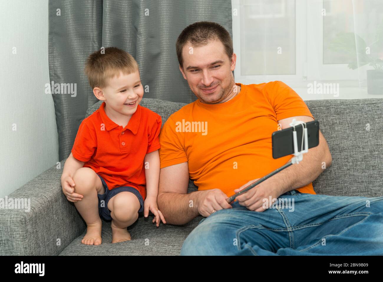 Junge und Mann, die während eines Online-Anrufs auf das Smartphone schauen und lächeln. Bleiben Sie zu Hause und Fernkommunikation Konzept Stockfoto