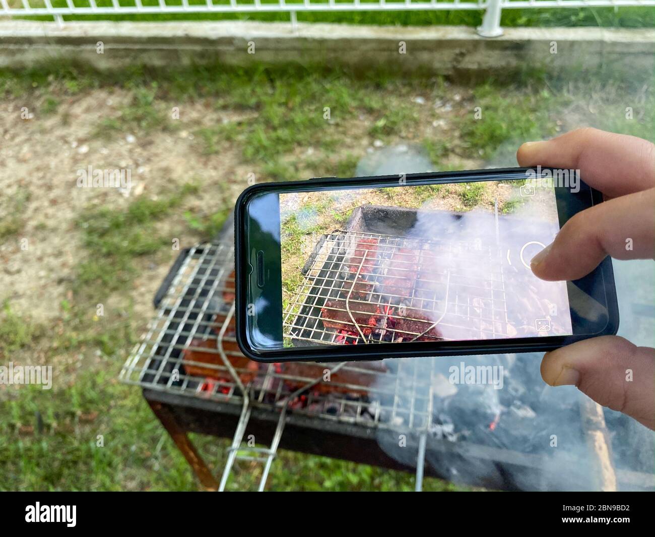 Mann, der mit seinem Handy ein Foto vom Grill machte. Leckeres gegrilltes Fleisch auf dem Grill - Türkische Wurst 'Sucuk' auf dem mangal in Natur Picknick Stockfoto