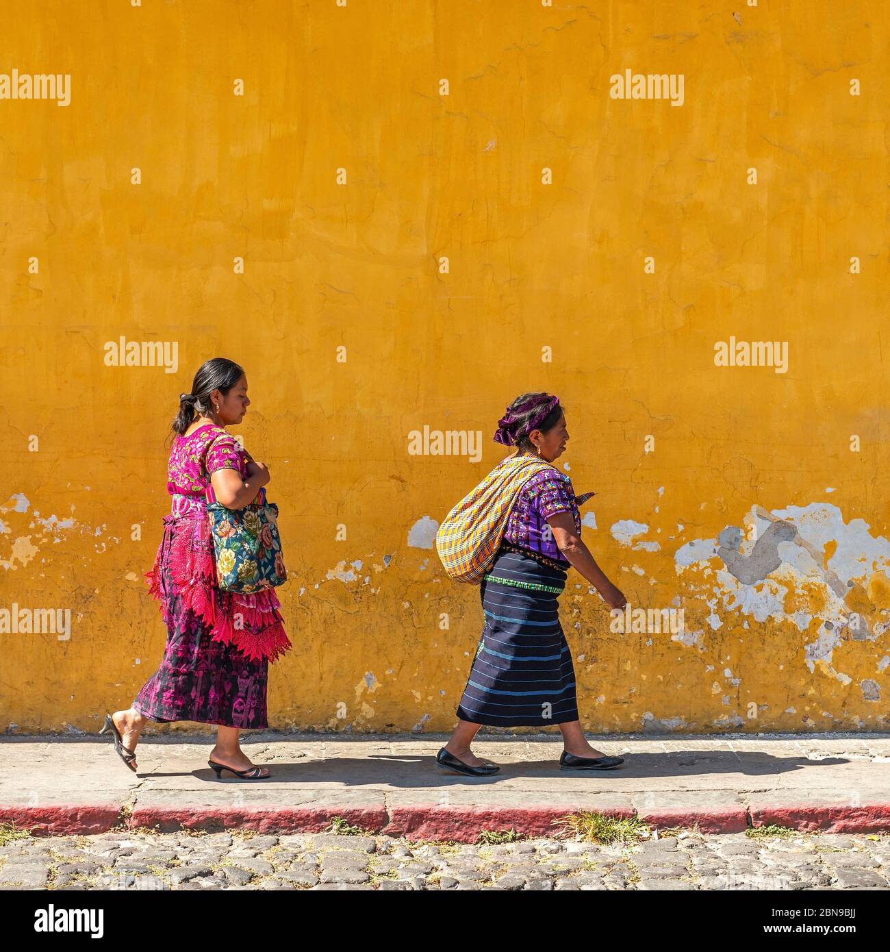 Indigene Maya-Frauen, die in traditionellen Kleidern durch die bunten Straßen von Antigua wandern, Guatemala. Stockfoto