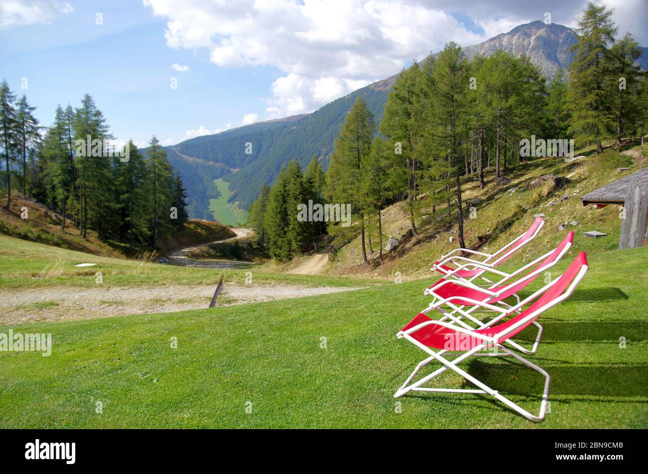 Rote Liegestühle zum Ausruhen Wanderer und bewundern Sie die hohen Berge mit grünen Wiesen und üppigen Wäldern und scharfen Felsen unter dem blauen Himmel Stockfoto