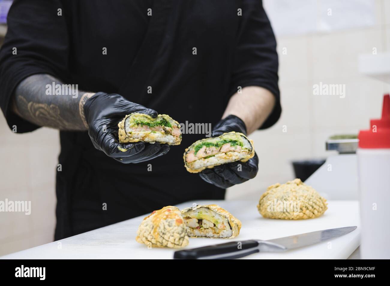 Frittierte Sushi-Burger in den Händen des Küchenchefs. Essen zum Mitnehmen, Fastfood Küche: Kochen in der gewerblichen Küche hält eine fertige Mahlzeit Stockfoto