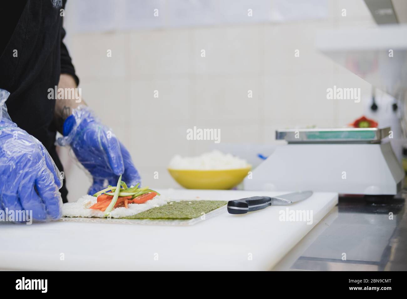 Die Hände eines Küchenchefs bereiten ein Sushi-Brötchen zu. Fast-Food-Küche, asiatische Lebensmittel, Essen zum Mitnehmen Zubereitung Stockfoto