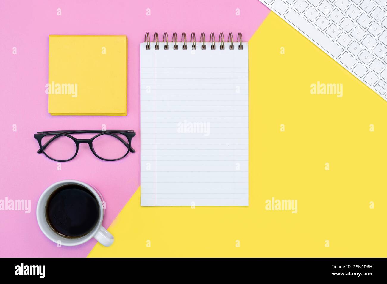 Rosa und gelbe Arbeitsplatz oder Online-Bildung Konzept. Notizblock. Schreiben. Kaffee, Tastatur, Gläser. Frühling Konzept. Stockfoto
