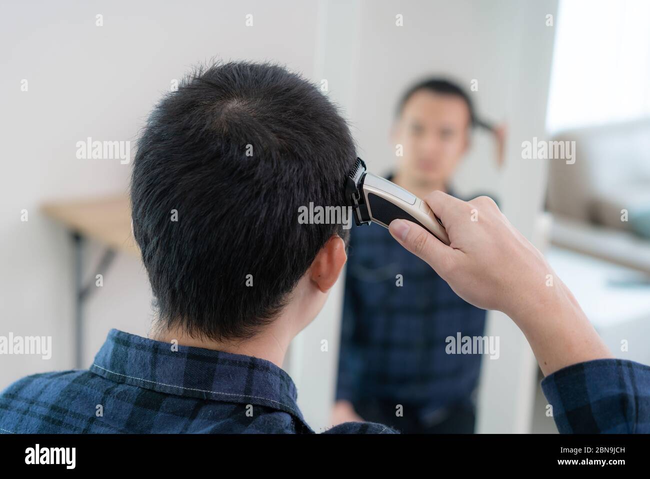 Asian Mann schneiden eigene seine Haare mit Haarschneideschere zu Hause bleiben sie zu Hause und Schutz in Ort während der Zeit der Isolation zu Hause gegen Roman Co Stockfoto
