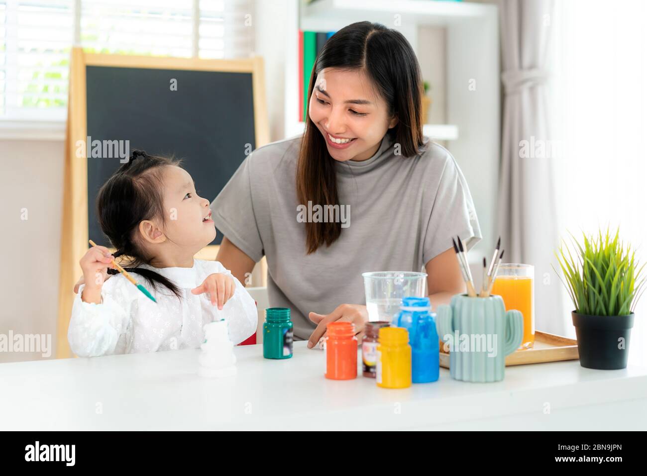 Asiatische Kindergarten Schulmädchen mit Mutter Malerei Gips Puppe mit Acryl Aquarell Farbe im Wohnzimmer zu Hause. Homeschooling und Abstand lear Stockfoto