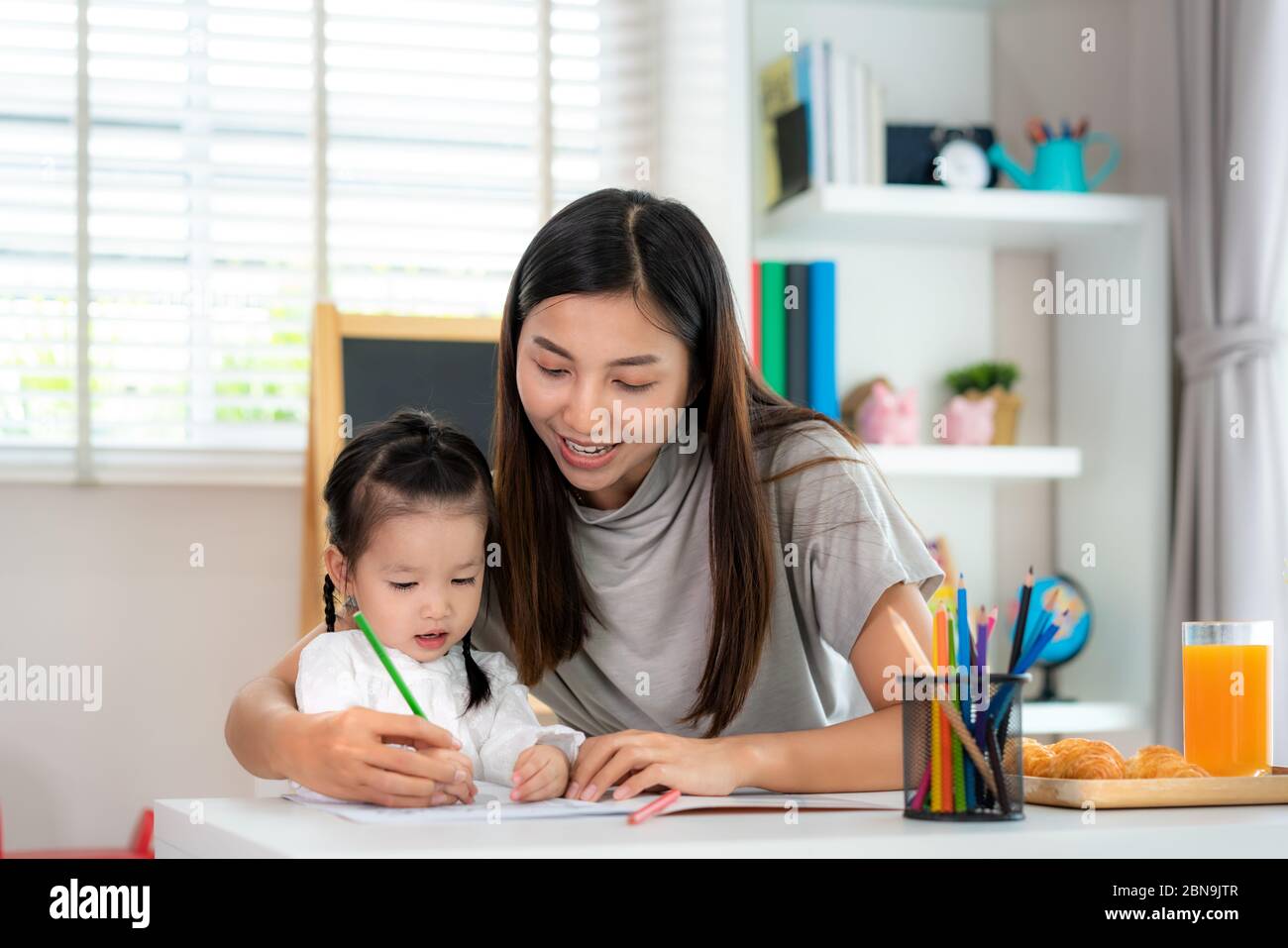 Asiatische Kindergarten Student Mädchen mit Mutter Malerei Bild in Buch mit Farbbleistift zu Hause, Homeschooling und Fernunterricht. Stockfoto