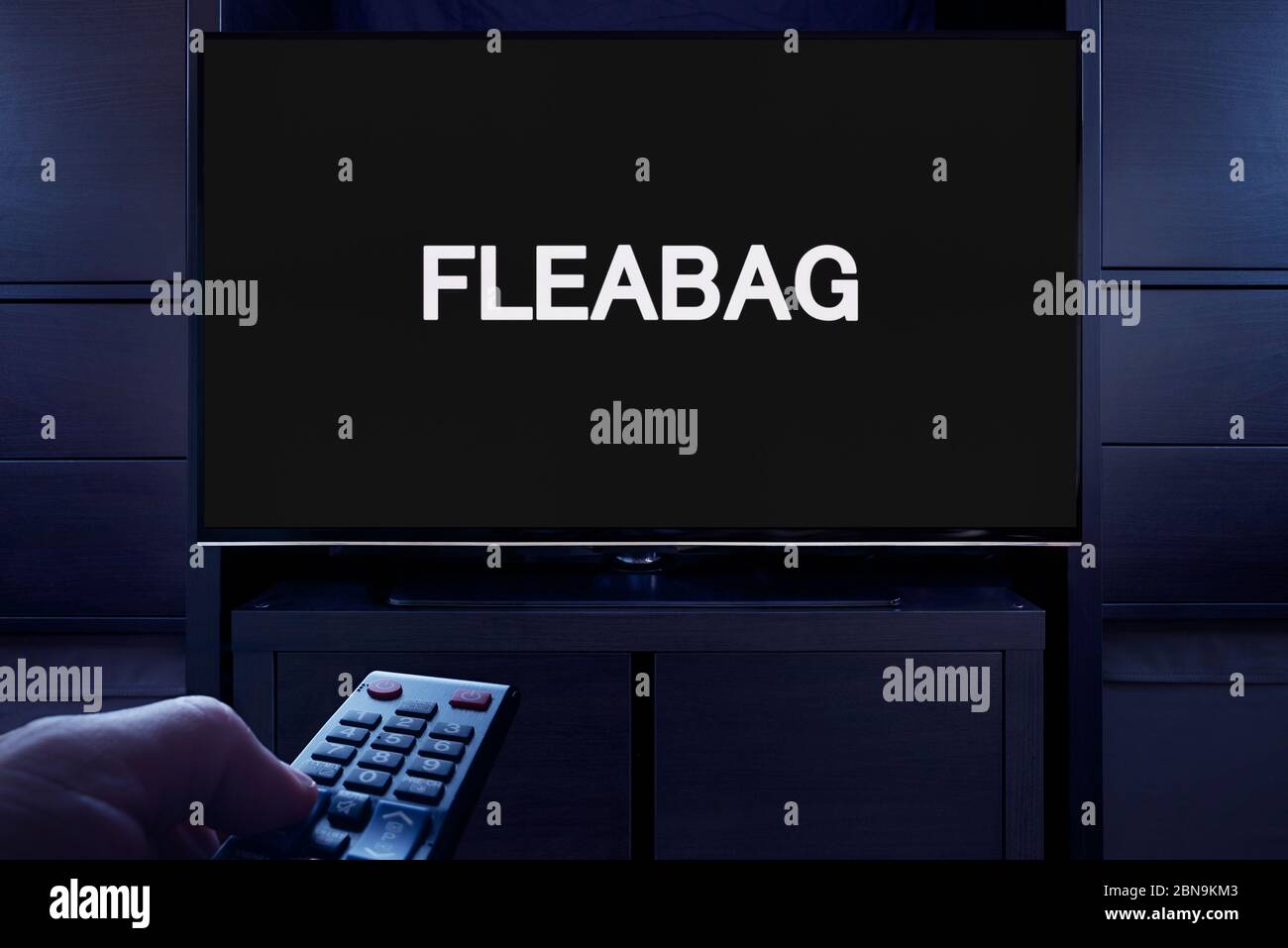 Ein Mann zeigt eine Fernbedienung auf den Fernseher, der den Hauptbildschirm des Fleabag anzeigt (nur redaktionelle Verwendung). Stockfoto