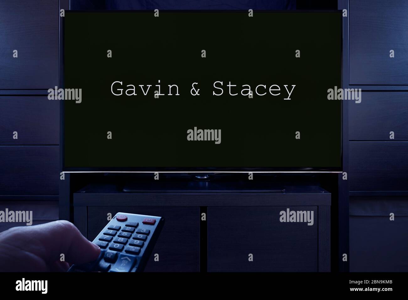 Ein Mann zeigt eine Fernbedienung auf den Fernseher, der den Hauptbildschirm von Gavin & Stacey anzeigt (nur redaktionelle Verwendung). Stockfoto