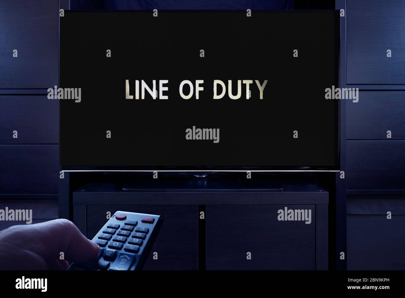 Ein Mann zeigt eine Fernbedienung auf den Fernseher, der den Hauptbildschirm der Line of Duty anzeigt (nur redaktionelle Verwendung). Stockfoto
