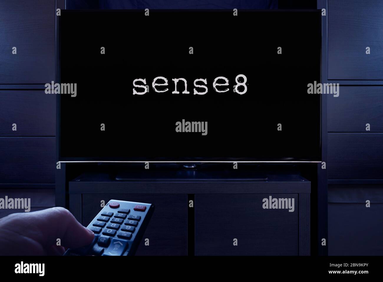 Ein Mann zeigt eine Fernbedienung auf den Fernseher, der den Hauptbildschirm von Sense 8 anzeigt (nur für redaktionelle Zwecke). Stockfoto