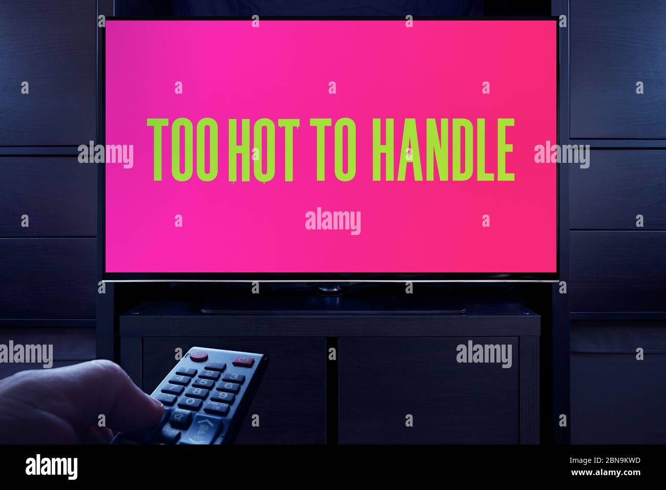 Ein Mann zeigt eine Fernbedienung auf den Fernseher, der den Bildschirm Too Hot to Handle (zu heiß, um den Haupttitel zu verwenden) anzeigt (nur redaktionelle Verwendung). Stockfoto