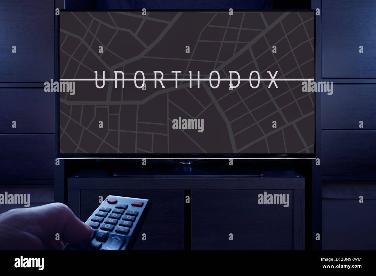 Ein Mann zeigt eine Fernbedienung auf den Fernseher, der den unorthodoxen Haupttitelbildschirm anzeigt (nur redaktionelle Verwendung). Stockfoto