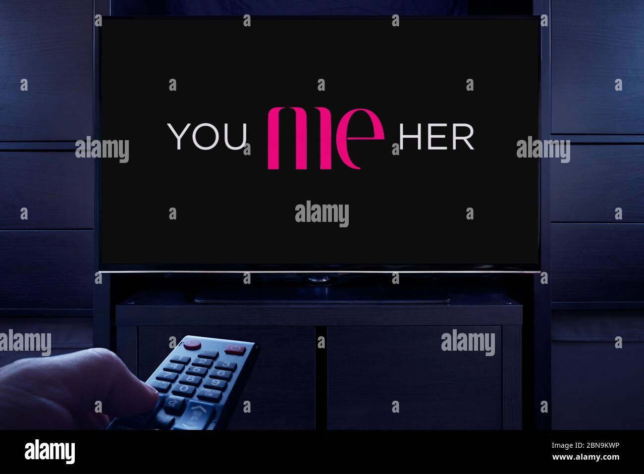 Ein Mann zeigt eine Fernbedienung auf den Fernseher, der den Hauptbildschirm von You Me (nur redaktionelle Verwendung) anzeigt. Stockfoto