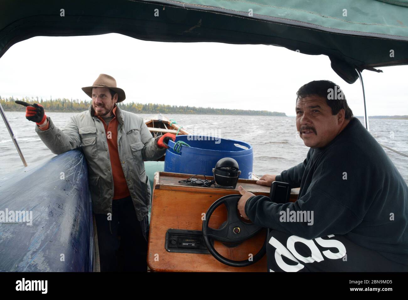 Ein indigener Mann aus Ojibwe steuert sein Boot mit einem Freund an Bord durch den Moose River in der Nähe der Stadt Moose Factory im Norden von Ontario, Kanada. Stockfoto
