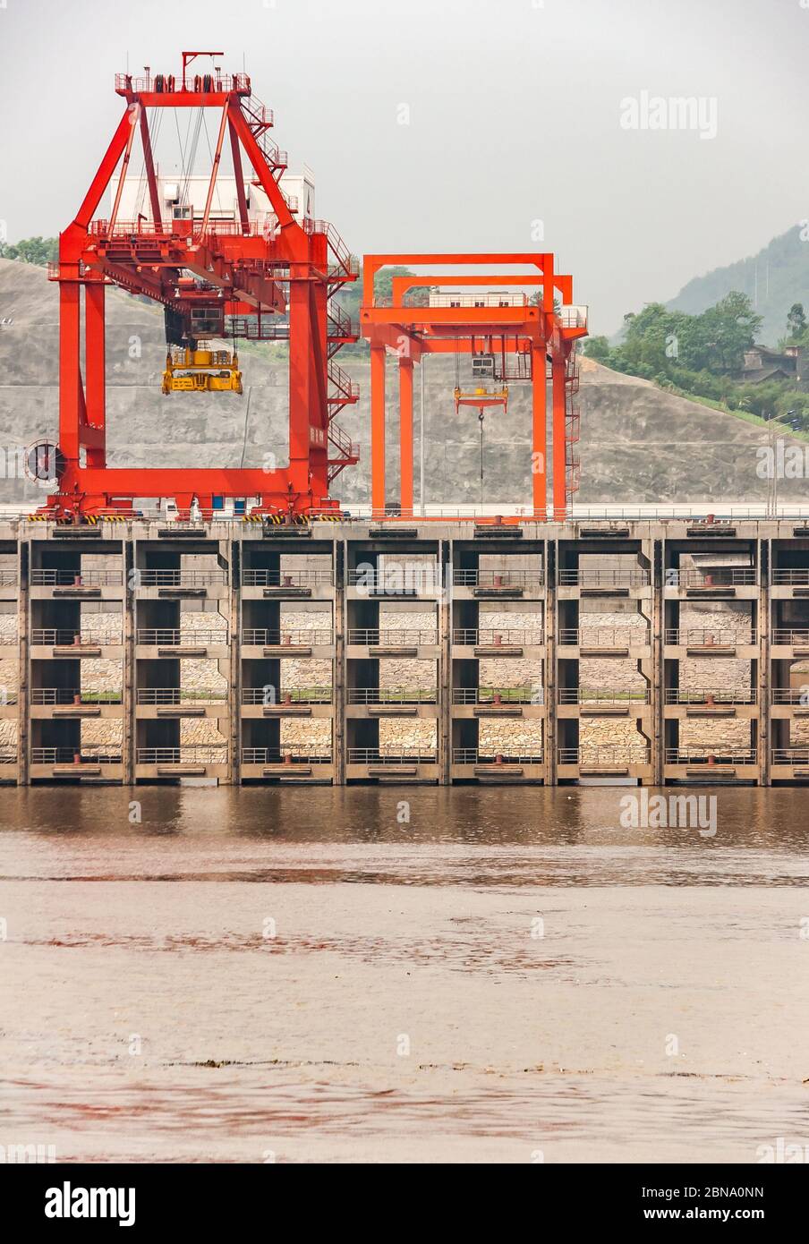 Huangqikou, Chongqing, China - 8. Mai 2010: Jangtse River. Nahaufnahme von roten Kranichen auf mehrstufigen Hafenquai hinter braunem Wasser. Hügel mit grünem Laub Stockfoto