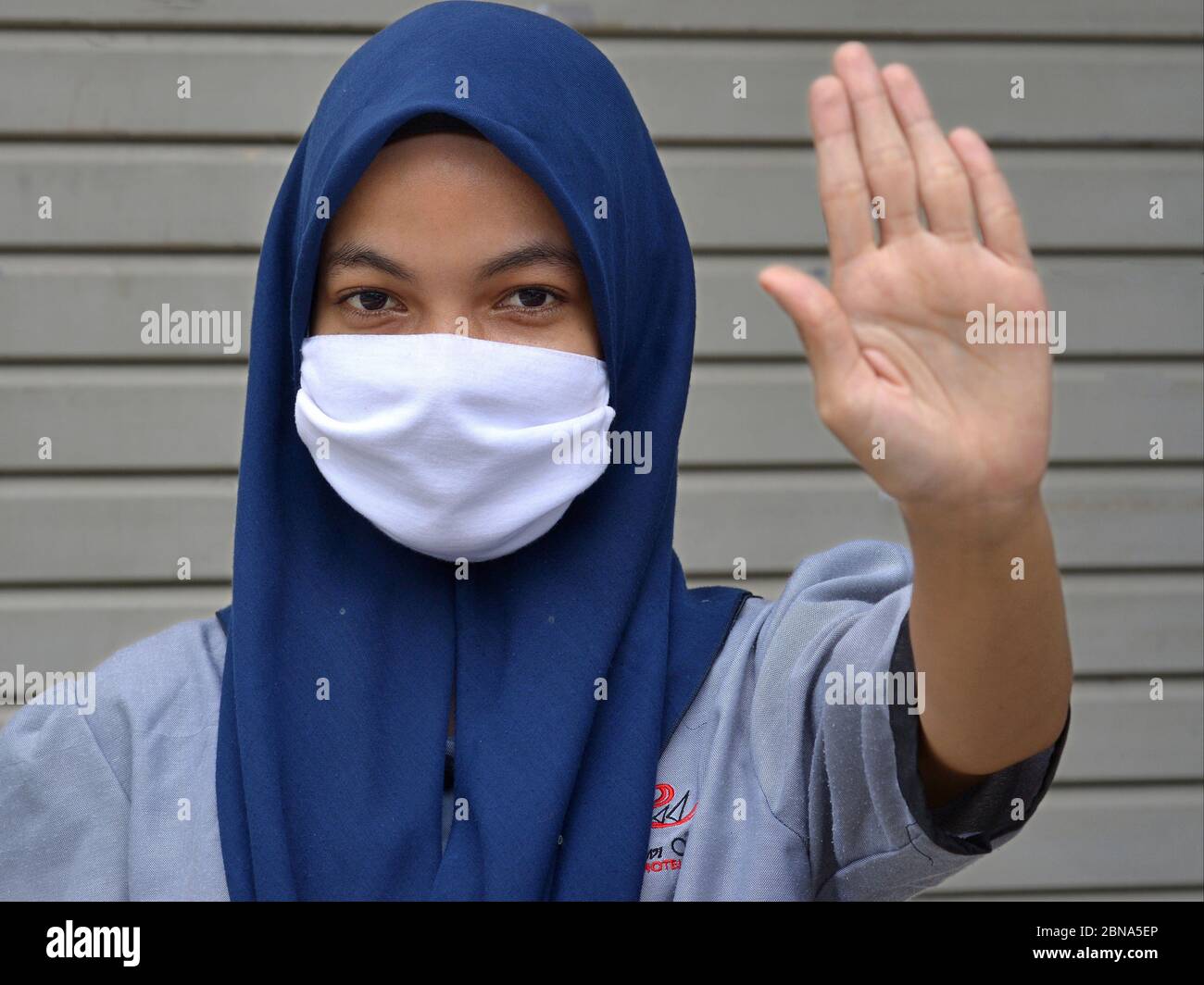 Muslimische malaiische Mädchen mit Hijab und Mund-Schleier macht Hand-Handfläche Stop-Zeichen während Corona Pandemie: Bleiben Sie weg! Stockfoto