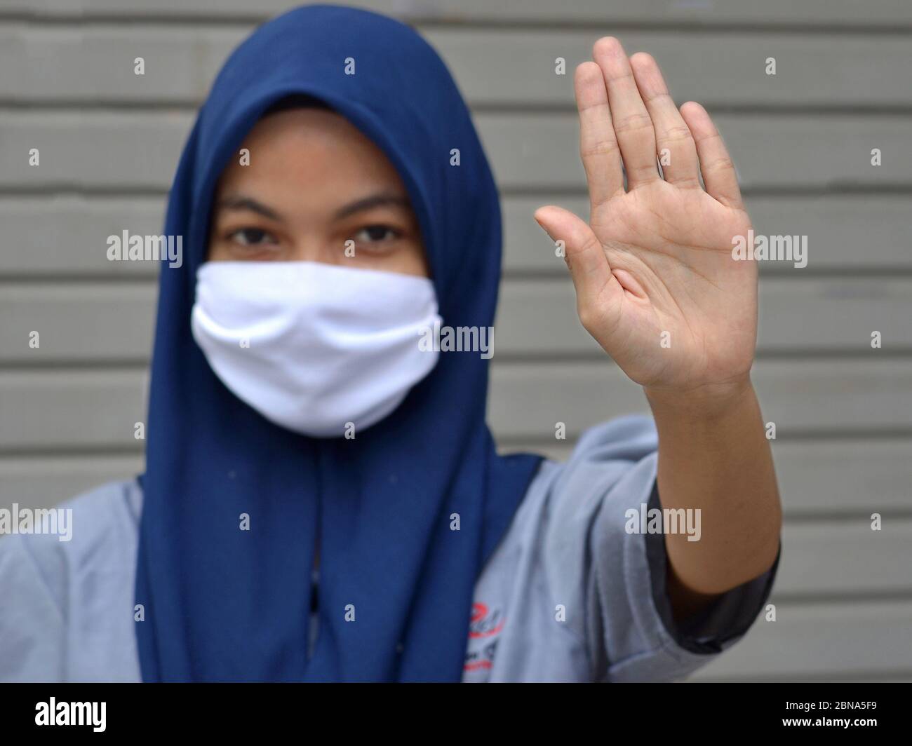 Muslimische malaiische Mädchen mit Hijab und Mund-Schleier macht Hand-Handfläche Stop-Zeichen während Corona Pandemie: Bleiben Sie weg! Stockfoto