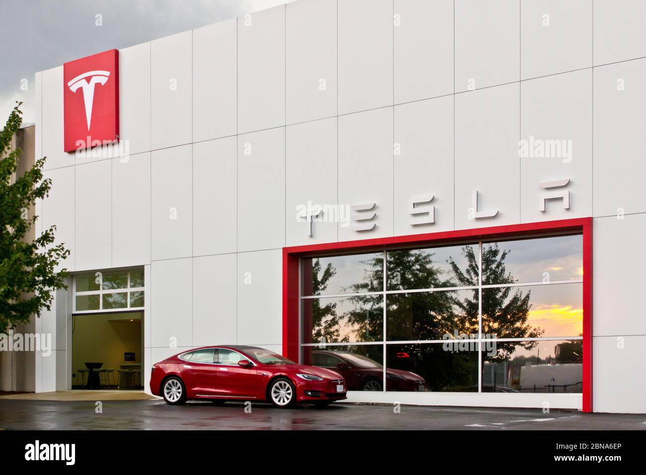 Außenansicht des Tesla Tysons Corner-Tyco Road Stores, Wien, Virginia, USA, mit rotem Model S Elektroauto vor dem Fenster, das den Sonnenuntergang nach dem Sturm reflektiert Stockfoto