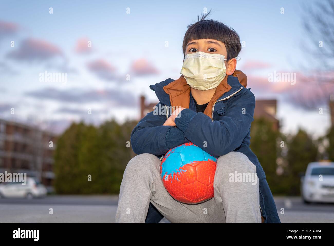 Kind spielt mit Fußball trägt Maske im Hinterhof während Roman Coronavirus Covid-19 Ausbruch und Quarantäne Stockfoto