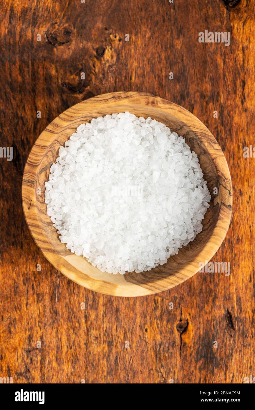 Weisses grobkörniges Salz in einer Schüssel auf einem Holztisch. Draufsicht. Stockfoto