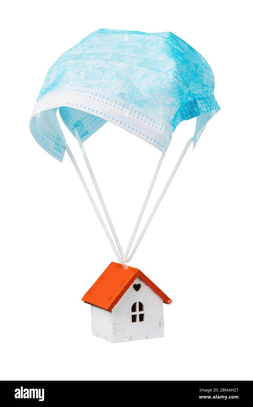 Ein Spielzeughaus fliegt auf einem Fallschirm von einer medizinischen Maske, isoliert auf weißem Hintergrund. Quarantäne-Exit-Konzept Stockfoto