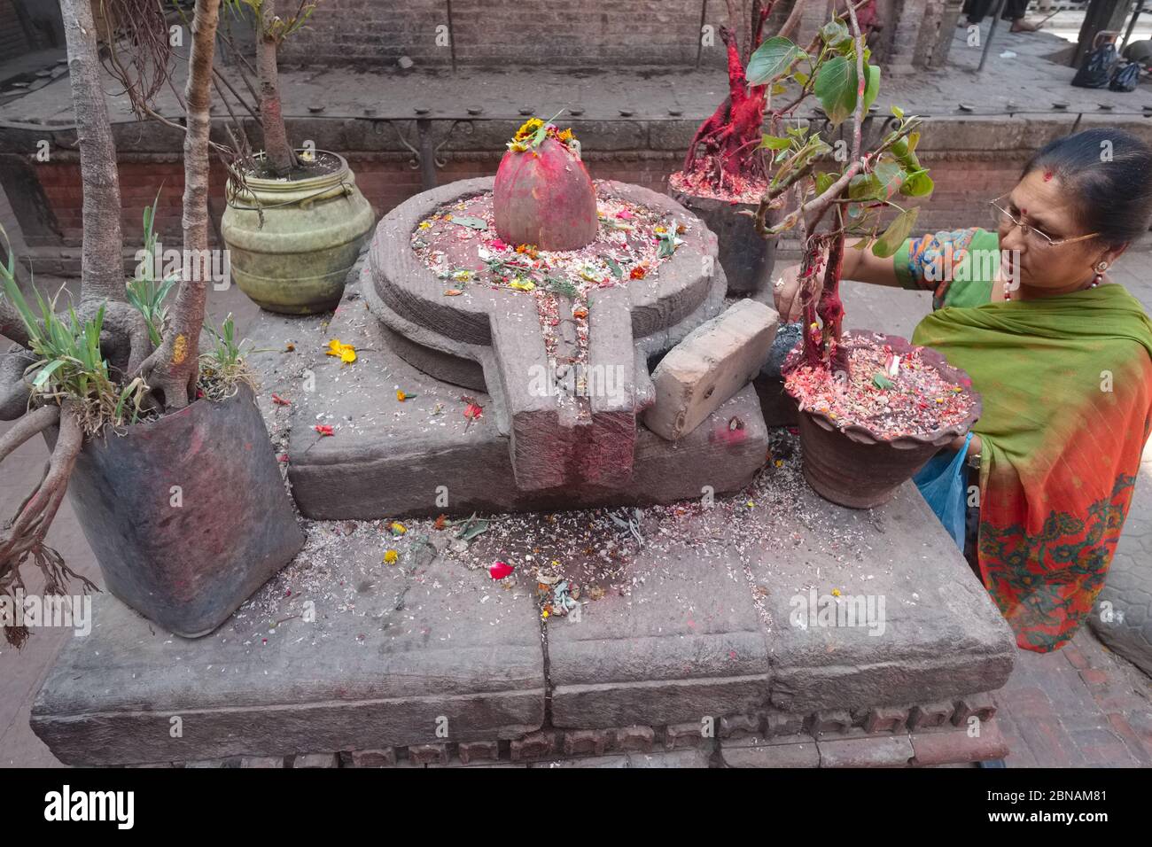 Eine Frau in Bhaktapur, Kathmandu Valley, Nepal, legt Blütenblätter auf einen Lingam und Yoni, die symbolische Darstellung von gott Shiva & Göttin Shakti Stockfoto