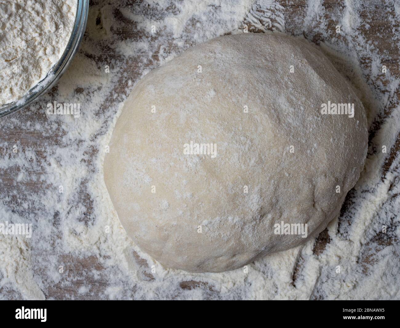Brotteig oder Pizzateig auf rustikalem Holzhintergrund mit Mehlstaubung. Stockfoto