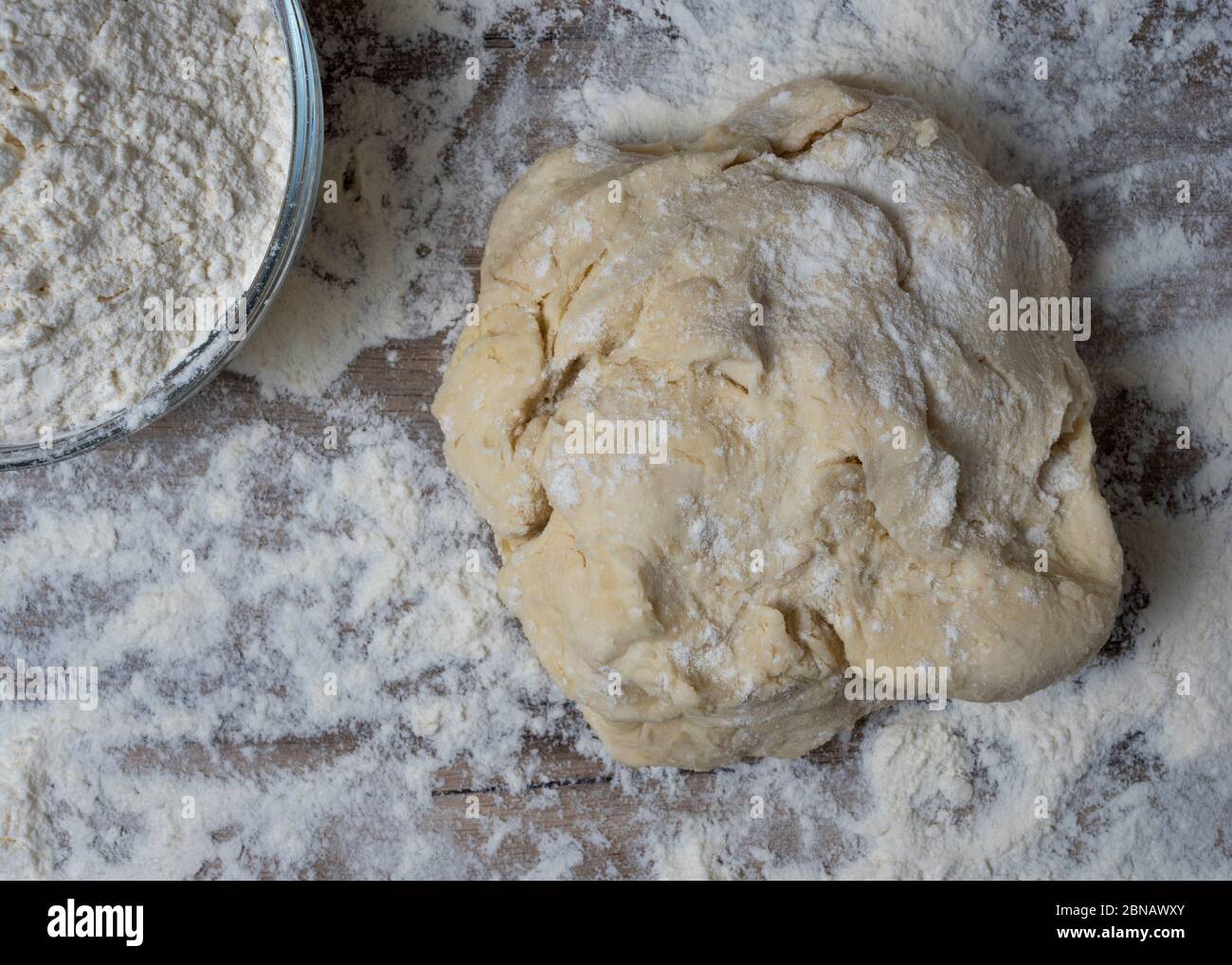 Rohes Brot oder Pizzateig auf rustikalem Holzhintergrund mit Mehlstaubung. Stockfoto