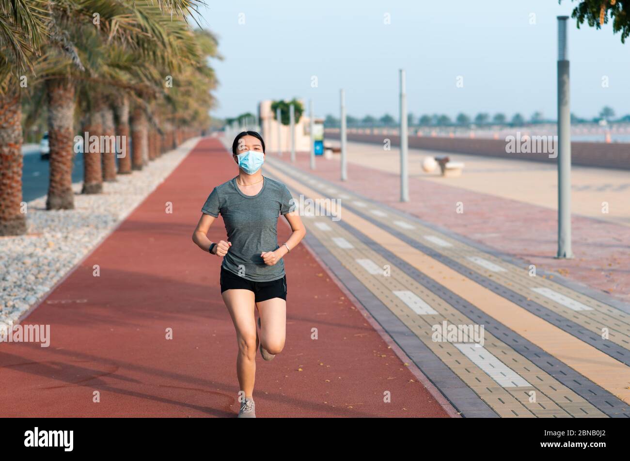 Asiatische Frau joggen auf der Laufstrecke tragen schützende chirurgische Maske, um die Ausbreitung des Coronavirus zu verhindern und sicher zu bleiben Stockfoto