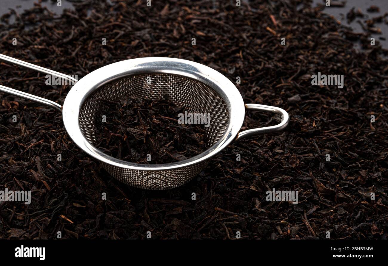 Teesieb aus Metall mit trockenen schwarzen Teeblättern Stockfoto