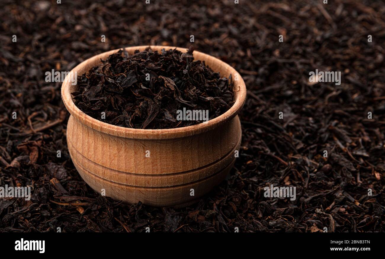 Trockene Teeblätter in Holzschüssel isoliert auf dunklem Hintergrund Stockfoto