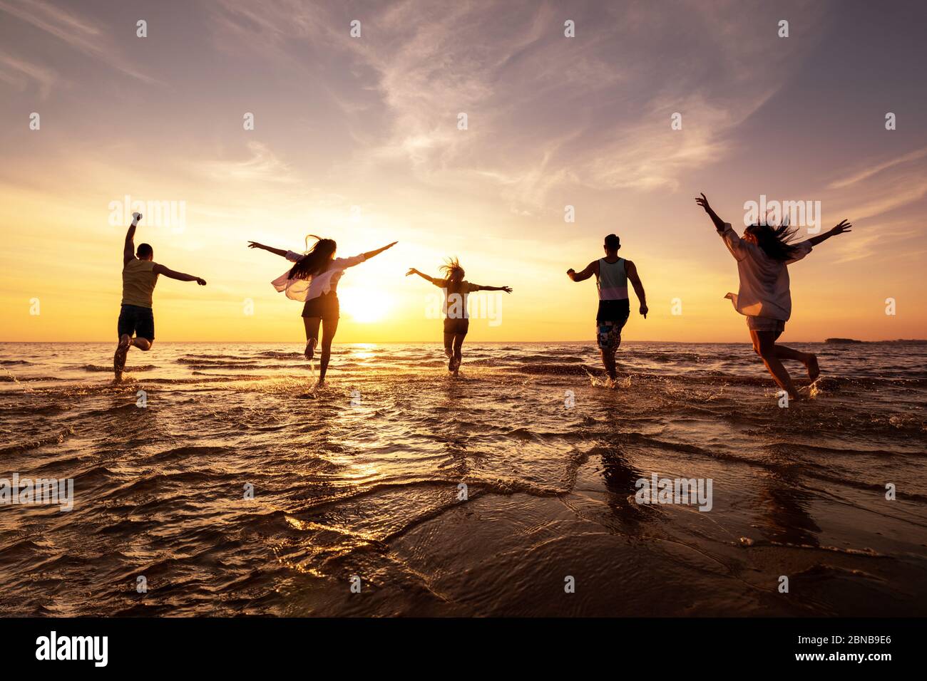 Fünf glückliche Freunde laufen mit erhobenen Armen am Sunset Beach Stockfoto