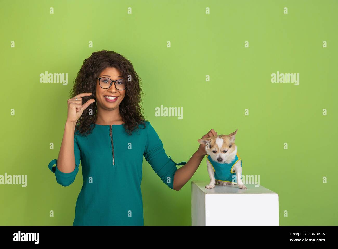 Zeigt etwas wenig mit den Fingern. afroamerikanische junge Frau Porträt isoliert auf grünem Hintergrund. Schönes Modell mit wenig doggy. Konzept der menschlichen Emotionen, Gesichtsausdruck, Verkauf, Anzeige. Stockfoto