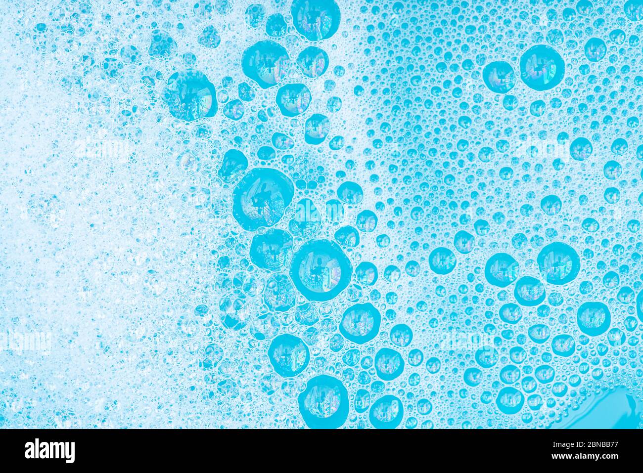 Nahaufnahme White Foam mit Blasen auf der Oberfläche des Wassers, Waschpulver mit Seife und blauem Bad, abstrakten Hintergrund transparente Blase. Stockfoto