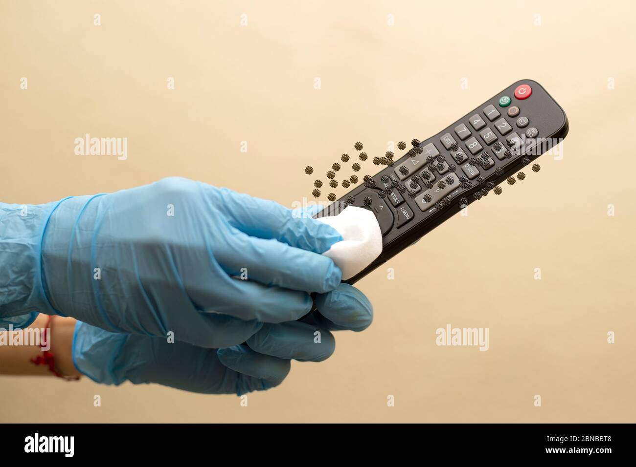 Frau, die die Fernbedienung des Fernsehers im Haus abwischt, blaue Handschuhe trägt und Desinfektionsmittel verwendet. Stockfoto