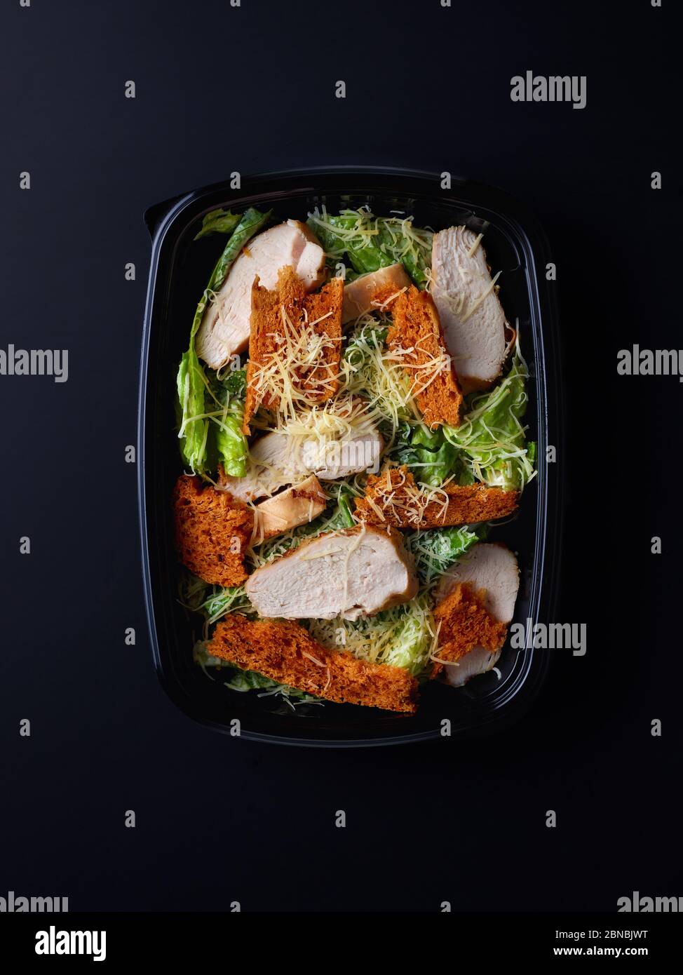Caesar Salat in schwarzer Kunststoffbox zum Mitnehmen, auf schwarzem Hintergrund, Draufsicht Stockfoto
