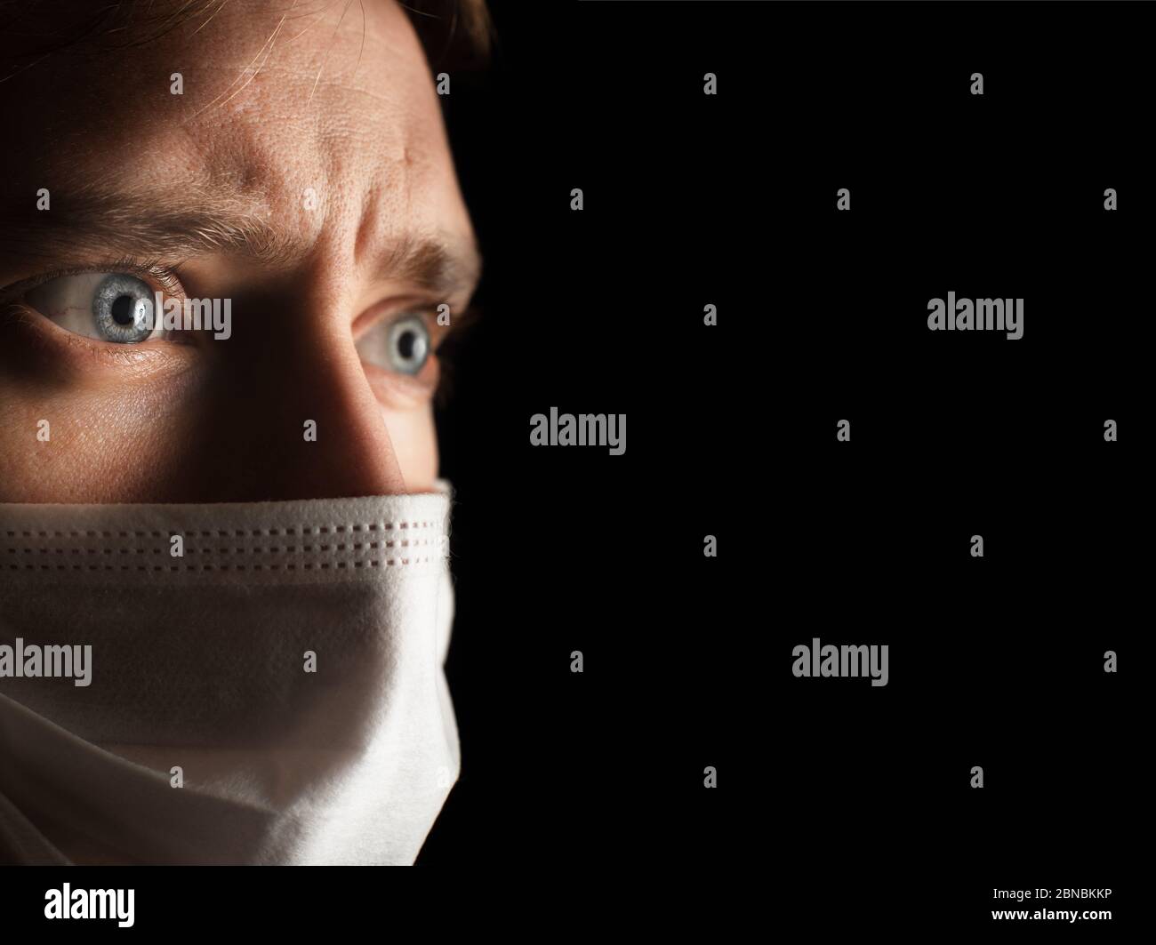 Kaukasischer junger Mann mit einer weißen Gesichtsmaske, die gerade schaut, mit einem Blick der Angst in seinen blauen Augen. Stockfoto