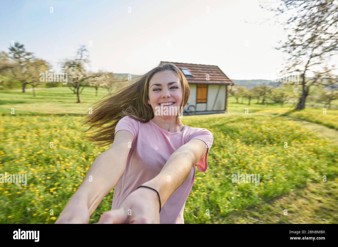 Junge glückliche Frau, tanzend auf dem deutschen Land im Hintergrund Wiesen, Bäume und ein Fachwerkhaus Stockfoto
