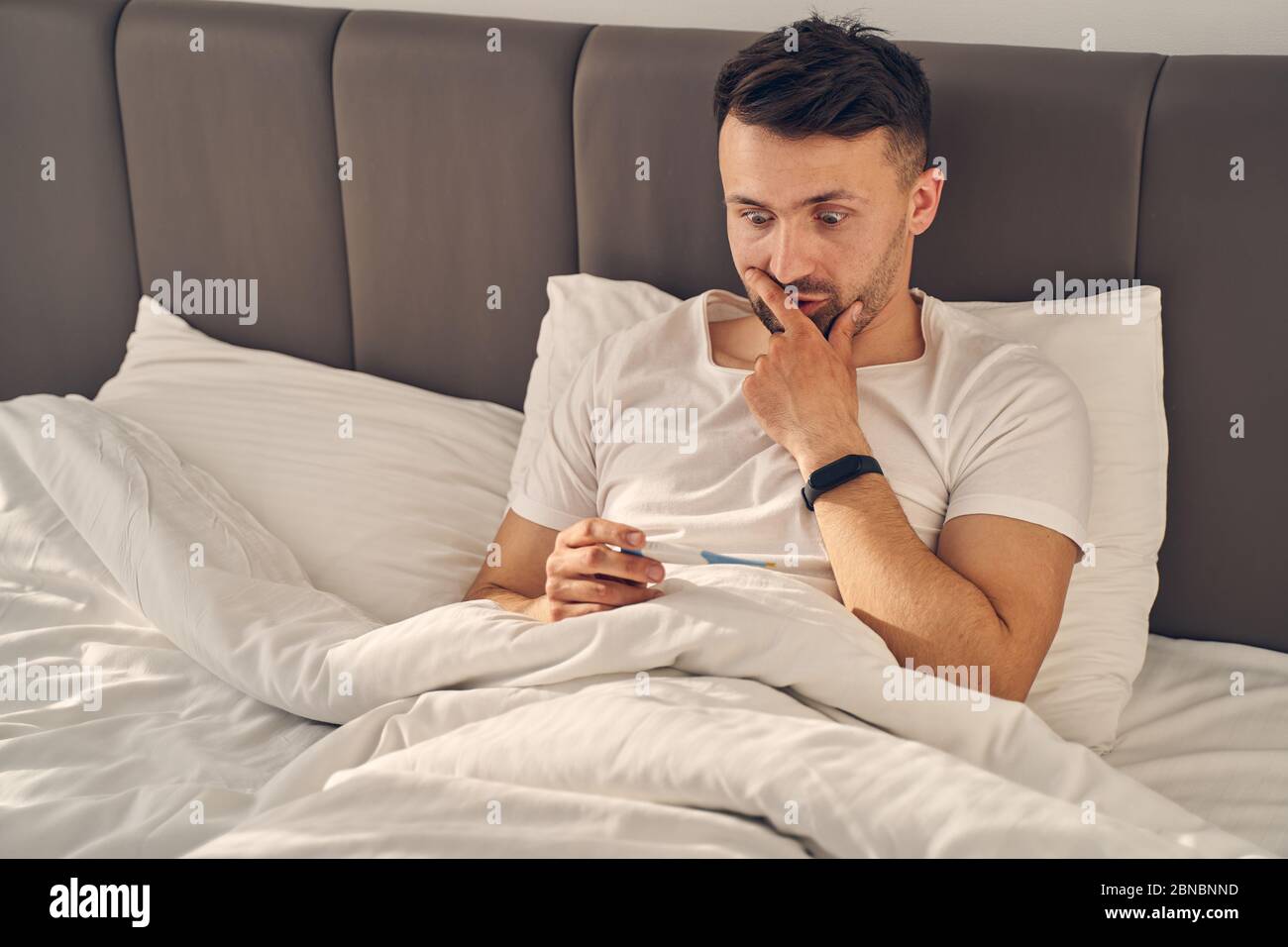 Mann, der im Bett blieb und überrascht aussschaute Stockfoto