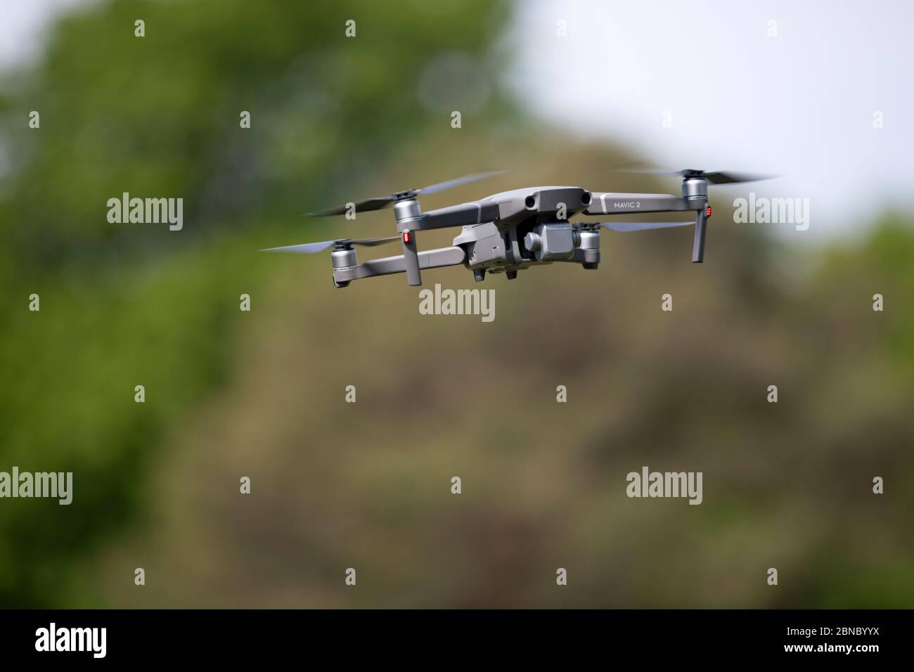 Moderne Drohne mit Kamera nach unten, die Landschaft erkundet, während sie im Sommer auf dem verschwommenen Hintergrund eines grünen Hügels in der Natur fliegt Stockfoto