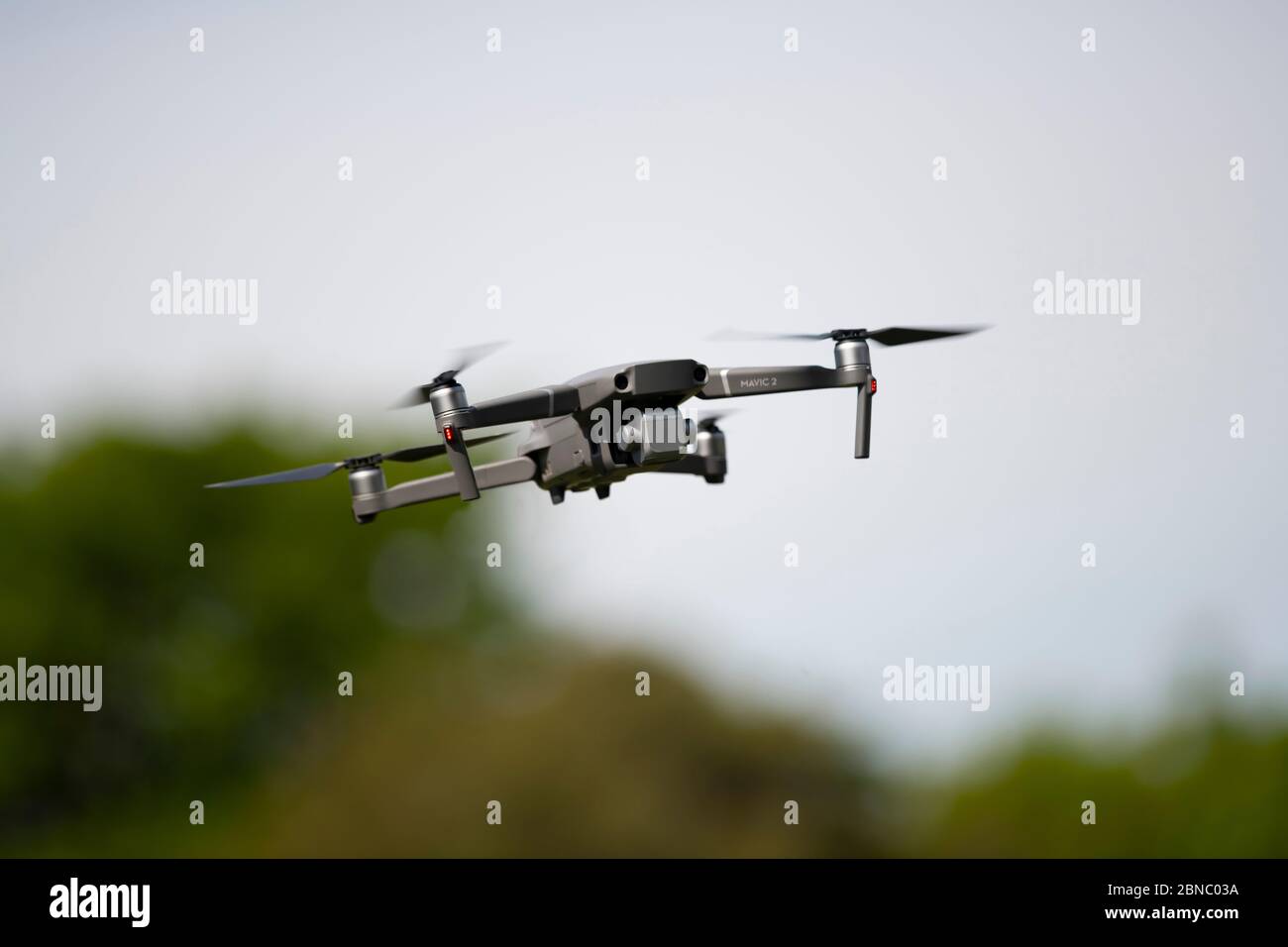 Moderne Drohne mit Propellern und Kamera nach unten fliegen auf verschwommenem Hintergrund von Büschen und Himmel während der Erkundung der Landschaft Stockfoto