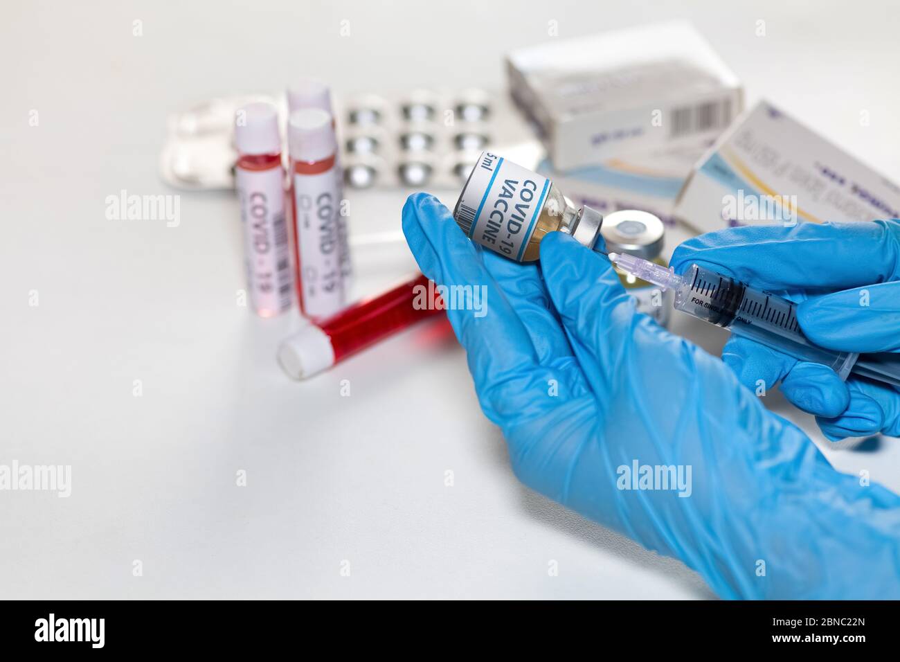 Hände eines Arztes in medizinischen Handschuhen, die eine hypodermische Nadel halten, die Medikamente aus einer Impfstoffflasche mit Blick auf Arzneimittel und Blutproben injiziert Stockfoto