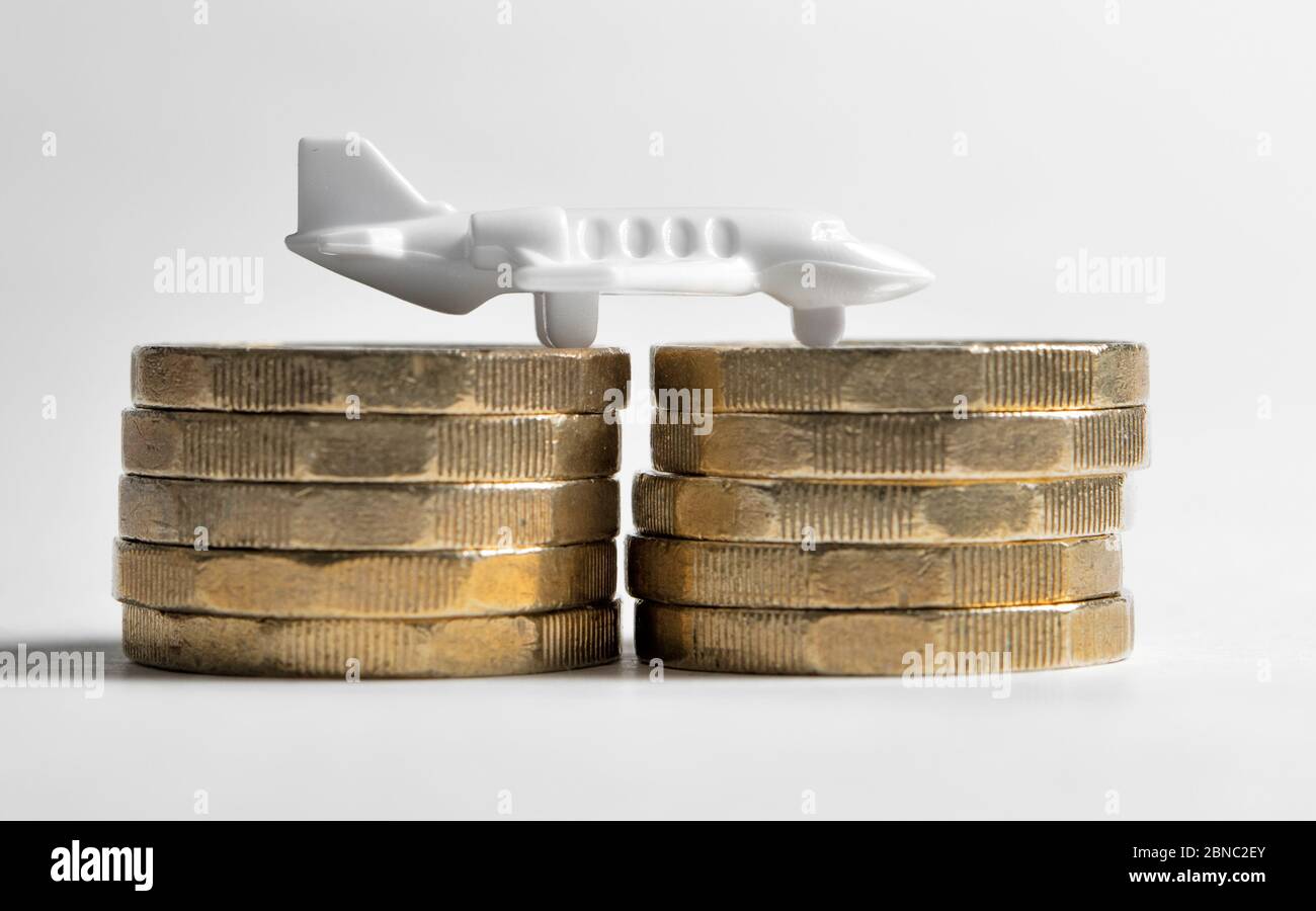 Kleines weißes Plastikflugzeug auf Stapel von Pfundmünzen vor einem weißen Hintergrund, Kosten des Flugreisekonzepts Stockfoto