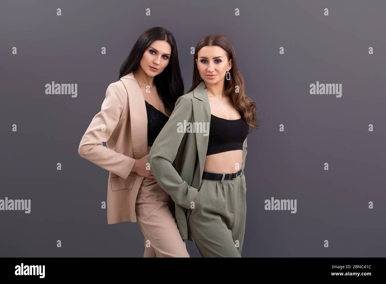 Porträt von zwei attraktiven Business-Frauen in Anzügen und Tops posiert auf grauem Hintergrund Stockfoto