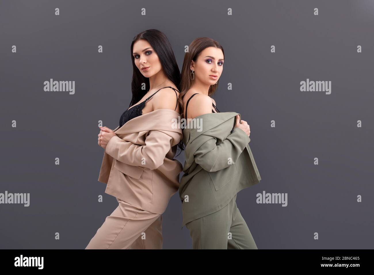 Porträt von zwei attraktiven Business-Frauen in Anzügen und Tops posiert auf grauem Hintergrund Stockfoto