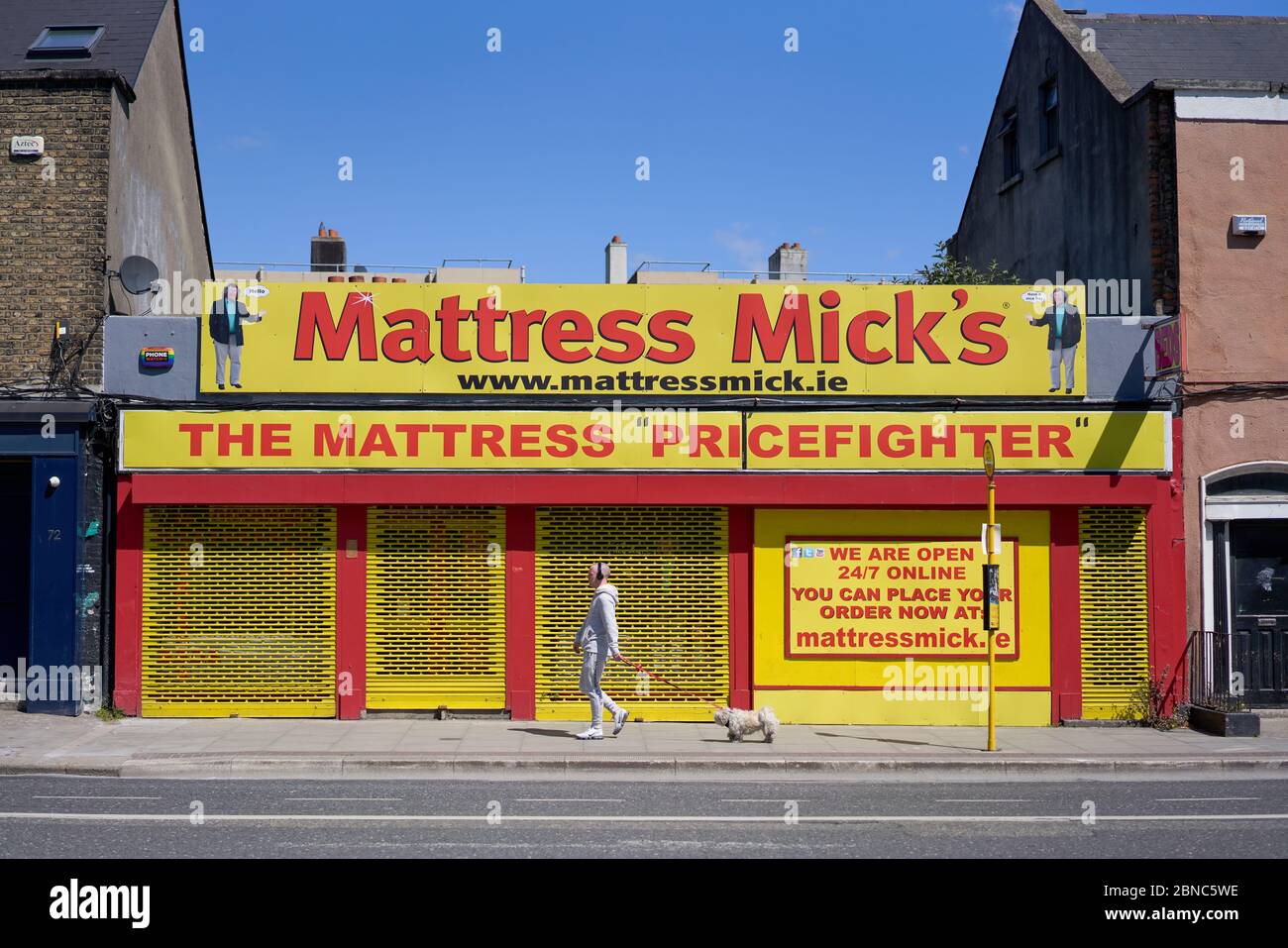 Ein Mann, der seinen Hund an einem Laden namens Mattress Micks in Dublin vorbeiläuft. Stockfoto
