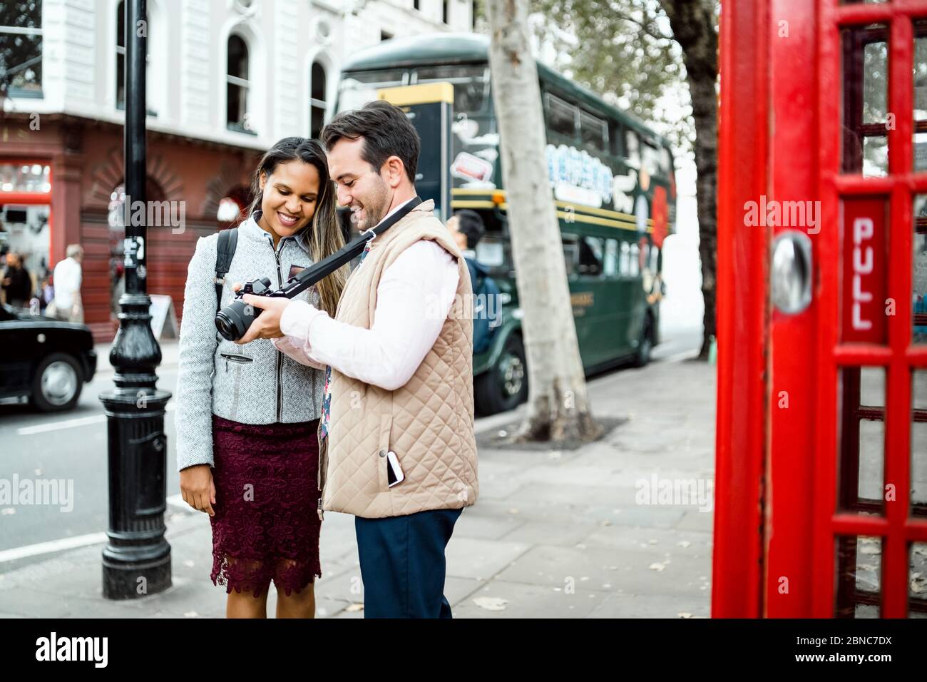Glücklich Reisen Paar Überprüfung Fotos auf ihrer Kamera in London, Großbritannien. Doppeldeckerbus und rote Telefonzelle in einem Rahmen Stockfoto