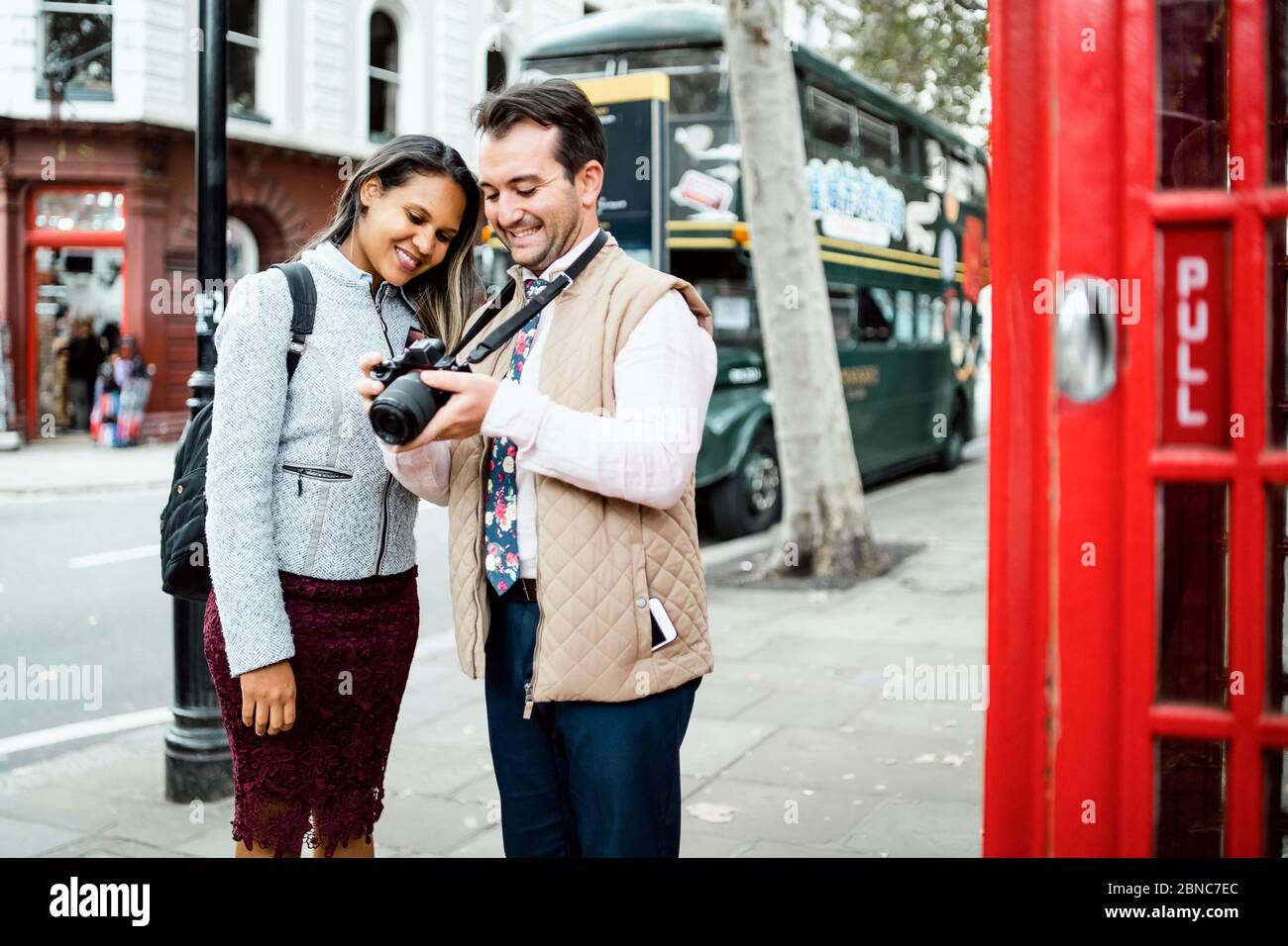 Glücklich Reisen Paar Überprüfung Fotos auf ihrer Kamera in London, Großbritannien. Doppeldeckerbus und rote Telefonzelle in einem Rahmen Stockfoto